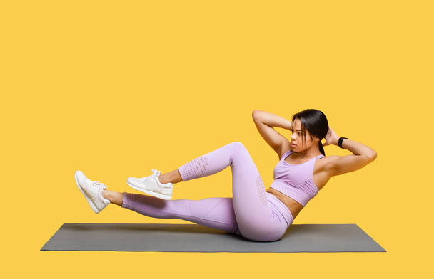 Doppio esercizio di crunch. Sporty donna afro-americana che lavora fuori, facendo esercizi addominali crunch bicicletta, sfondo giallo - Foto, immagini