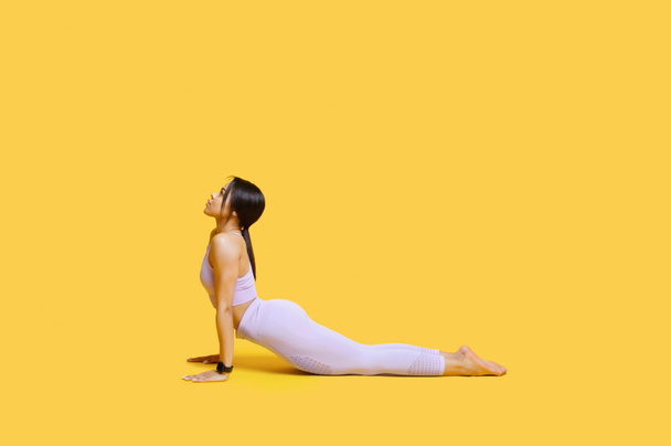 Working out. Young black woman practicing yoga, doing Cobra exercise, staying in Bhujangasana pose, yellow background - Φωτογραφία, εικόνα