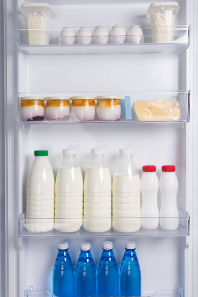 in the door of the white refrigerator, on the shelf are eggs, cheese, yogurt, cottage cheese, milk and bottled water - Foto, afbeelding