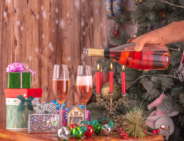 男性は新年の木の背景を背景にシャンパンのフルートにボトルからシャンパンを注ぐ手とプレゼント. - 写真・画像