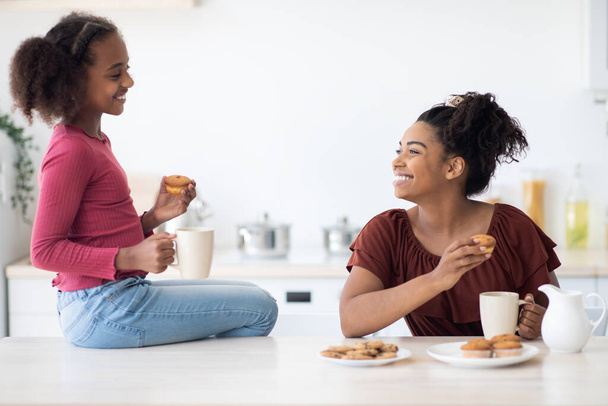 Cheerful african american mom and daughter drinking tea with cupcakes - Foto, immagini