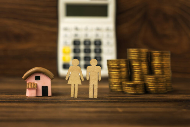 Twee figuren van mensen, een huis en munten op de achtergrond van een rekenmachine. Het concept van woningaankoop. Hypotheek. - Foto, afbeelding