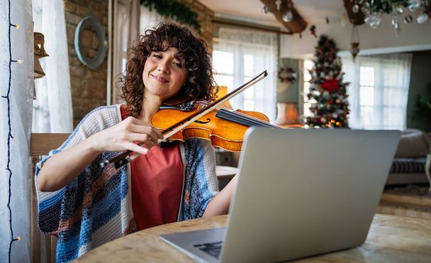 Woman music teacher talking with a student and giving instructions, teaching how to play a song the violin online during a video call - Photo, Image