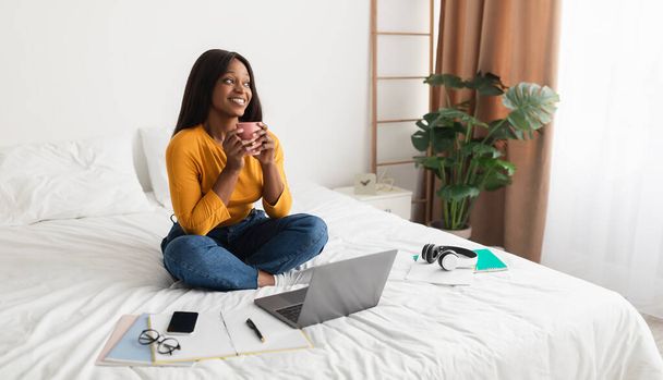 Panorama 'da Afro-Amerikalı Kadın Laptop kullanıyor. Kahveyi zevkle içiyor. - Fotoğraf, Görsel