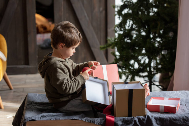 Küçük çocuk masada oturuyor ve evde Noel hediyeleriyle oynuyor.  - Fotoğraf, Görsel
