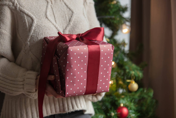 Γυναίκα κρατά ένα κόκκινο χριστουγεννιάτικο δώρο στα χέρια - Φωτογραφία, εικόνα