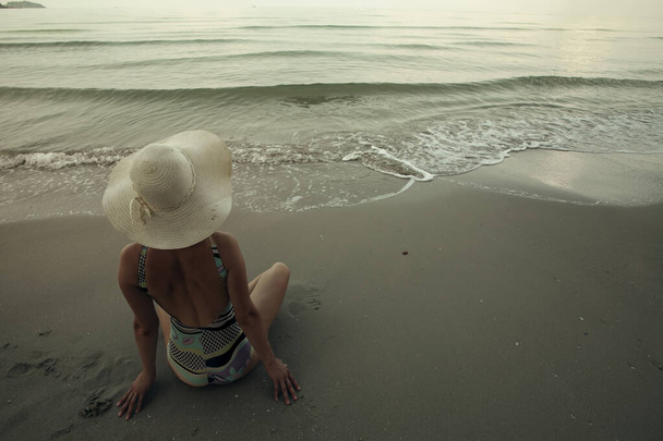 Una donna riposa sulla spiaggia tropicale del mare. Seduto in un cappello panama vista posteriore. - Foto, immagini