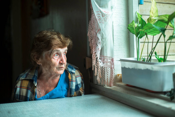 Portrait of pensive elderly woman sadly looking out the window. - Фото, изображение