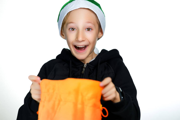 A cheerful boy in a green Santa hat holds a yellow bag - Photo, Image