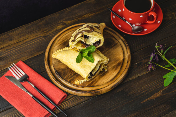 Snídaně se sladkou čokoládou sendvič velikosti calzone a káva podávaná na tmavém dřevěném stole. - Fotografie, Obrázek
