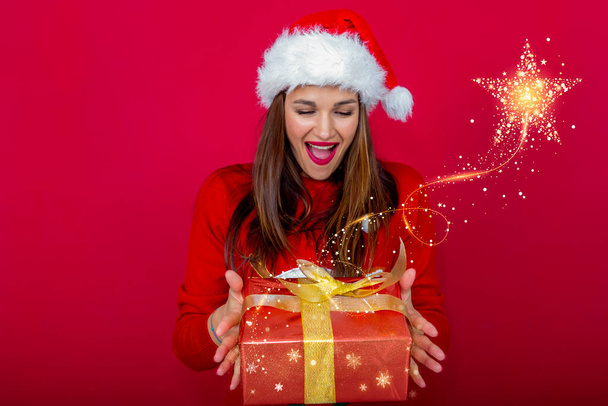 милая и красивая женщина с шляпой Санта-Клауса и подарочной коробкой в руках. Удивлённое лицо и яркая рождественская звезда. - Фото, изображение
