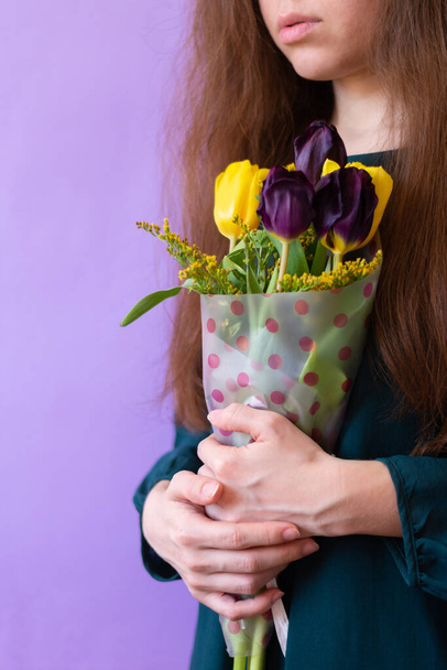 Woman of caucasian ethnicity holds bunch in wrapping paper with fragile spring tulips.Vertical format.Copy space on purple background - Foto, Imagem
