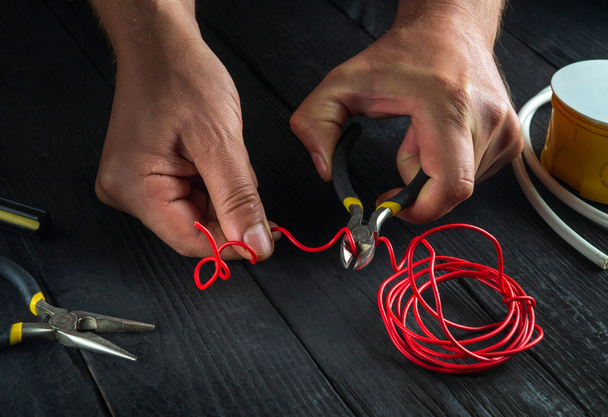 Close-up of hand of electrician foreman while working or cutting red wire. Repair of electrical equipment in the workshop of master electrician - Fotografie, Obrázek