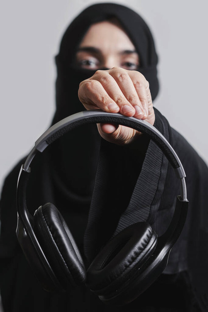 ヒジャーブのイスラム教徒の女性はヘッドフォンを - 写真・画像