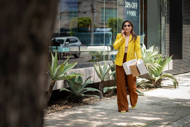 jong vrouwelijk winkelen executive dragen haar tassen terwijl praten op mobiele telefoon - Foto, afbeelding