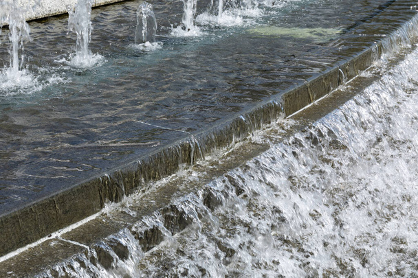 Água borbulhando de várias cabeças de fonte em uma piscina pública, descendo escadas em cascata, aspecto horizontal - Foto, Imagem