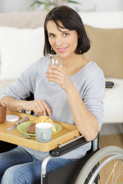 señora en silla de ruedas en casa comiendo comida de una bandeja - Foto, imagen