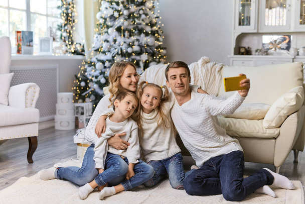 Noël, vacances, concept de technologie et de personnes - famille heureuse assise dans le salon et prenant des photos selfie avec smartphone à la maison - Photo, image