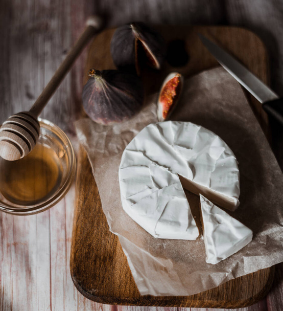 Queso Camembert con higos, cariño. Brie redondo o queso camembert en la tabla de cortar blanco con frutas. Enfoque selectivo - Foto, imagen