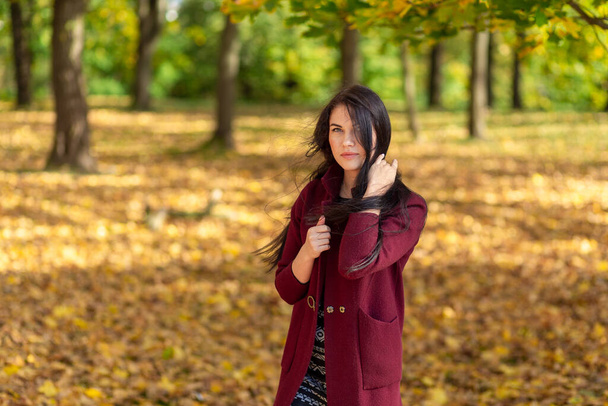 Portret van een vrolijke jonge vrouw die geniet in het herfstpark. Mooi brunette meisje in de herfst rode jas en zwarte trui. Ontspan in de natuur. Hoge kwaliteit foto - Foto, afbeelding