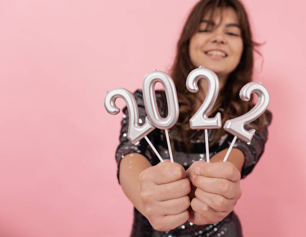 Een vrolijk meisje op een roze achtergrond houdt de nummers 2022 in haar handen. - Foto, afbeelding