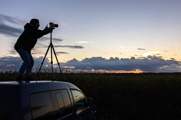 Das Mädchen auf dem Autodach fotografiert den Sonnenuntergang mit einem Stativ. - Foto, Bild
