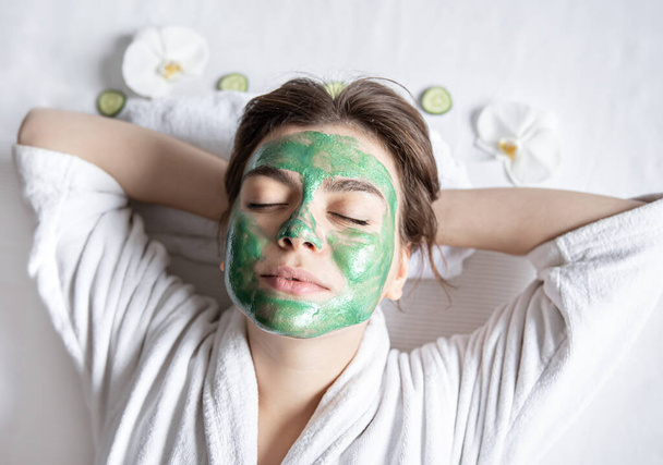 Jeune femme avec un masque cosmétique sur le visage se repose couché, vue du dessus. - Photo, image