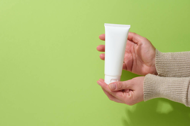la mano femenina sostiene tubos vacíos de plástico blanco para cosméticos. Embalaje para crema, gel, suero, publicidad y promoción de productos, maqueta - Foto, Imagen