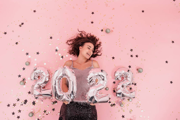 Een meisje op een roze achtergrond met zilveren ballonnen uit nummer 2022, bovenaanzicht. - Foto, afbeelding