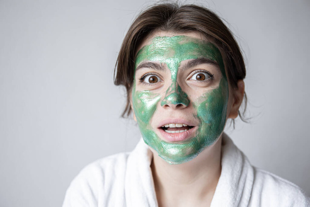 Ελκυστική νεαρή γυναίκα με πράσινη καλλυντική μάσκα στο πρόσωπό της. - Φωτογραφία, εικόνα