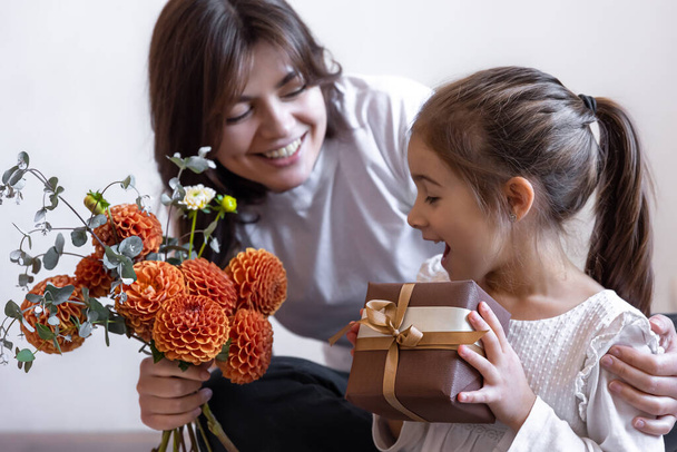 Ein kleines Mädchen überreicht ihrer Mutter ein Geschenk und einen Blumenstrauß. - Foto, Bild