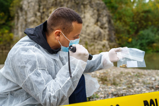 Forensic police investigator collecting evidence at the crime scene by the river in nature copy space in day - Photo, image