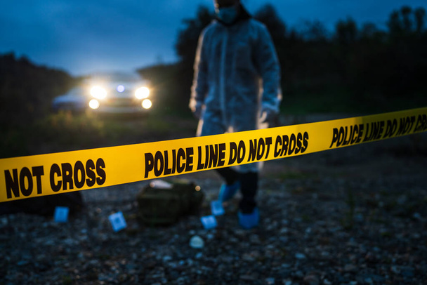 Forensic police investigator collecting evidence at the crime scene by the river in nature at night selective focus on police line tape - Photo, Image