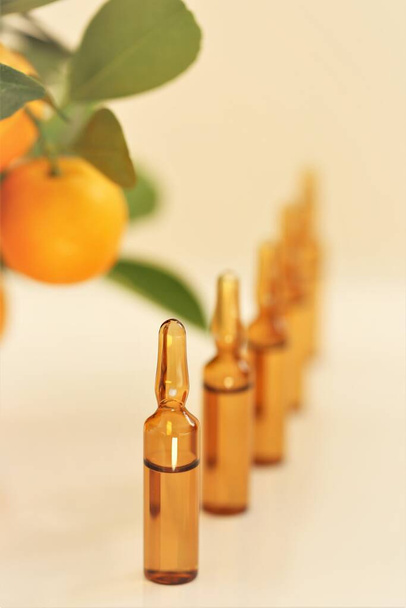 Vitamin C. sérum s vitamínem C.Skleněné ampulky a mandarinky na béžovém pozadí.Ampule a sérum s vitamínem C.Zdraví a krása. Organická přírodní kosmetika. - Fotografie, Obrázek