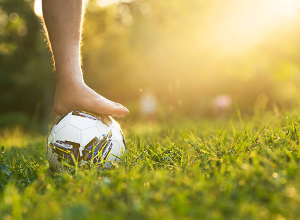 Male foot without shoes on a soccer ball on a grassy field with a sun glare and a copy space. - Foto, Imagen