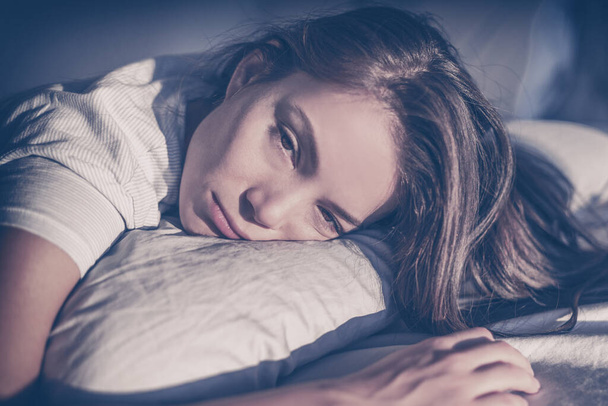 Insomnia late at night in TV blue light dark bedroom depressed tired young Asian woman lying on pillow bed sleepless with funny expressive unhappy sad face - Fotoğraf, Görsel