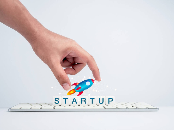 Startup concept. Hand holding rocket on white dice blocks with the word, startup on keyboard computer on a white desk and white background. Success creative motivation for business innovation. - Foto, imagen