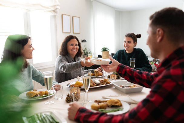 成熟した白人女性は家族の間に若い男に食べ物のプレートを渡しますクリスマスディナー. - 写真・画像