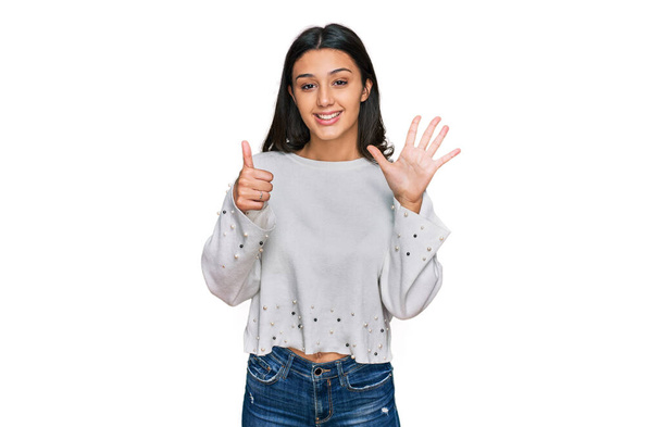 Joven chica hispana usando ropa casual mostrando y señalando con los dedos número seis mientras sonríe confiado y feliz.  - Foto, Imagen