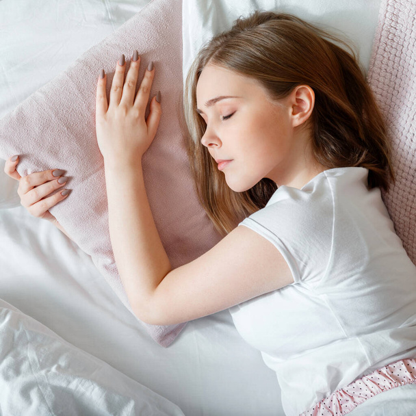 Young Woman sleeping in bed. Portrait of blonde teen girl have healthy good sleep on white pink pillow. Teenager girl in pajamas sleeps in bedroom at morning time. Top view square - Foto, immagini