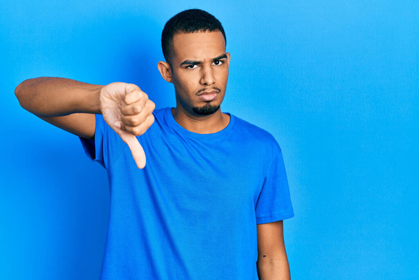 Junger afrikanisch-amerikanischer Mann in lässigem blauem T-Shirt, der unglücklich und wütend aussah und Ablehnung und Ablehnung mit Daumen nach unten Geste zeigte. Schlechte Miene.  - Foto, Bild