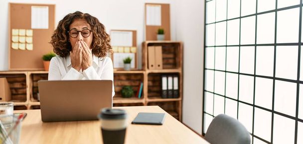 Латиноамериканка средних лет, работающая в офисе в очках, скучает зевая от усталости, прикрывая рот рукой. беспокойство и сонливость.  - Фото, изображение