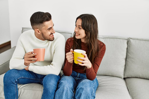Mladý hispánský pár pití kávy sedí na pohovce doma. - Fotografie, Obrázek