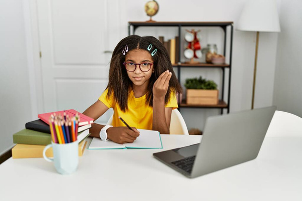 Young african american girl doing homework at home doing italian gesture with hand and fingers confident expression  - Photo, image