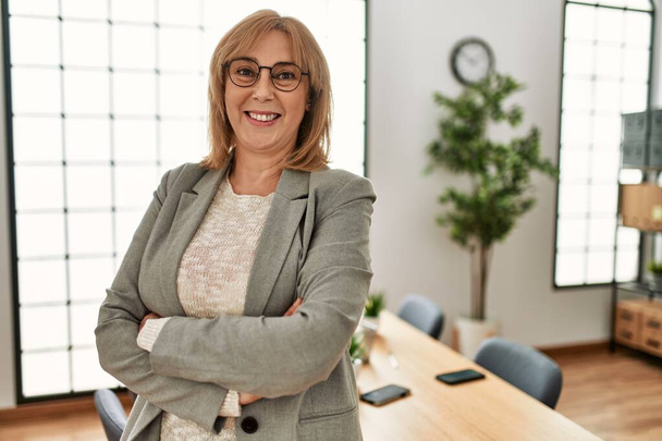 Middle age businesswoman smiling happy standing with arms crossed gesture at the office. - Foto, Bild