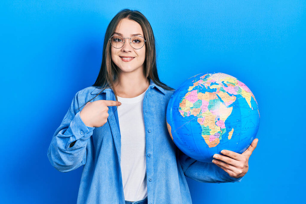Young hispanic girl holding world ball pointing finger to one self smiling happy and proud  - Фото, зображення