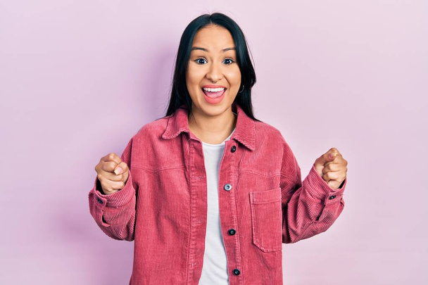 Beautiful hispanic woman with nose piercing wearing casual pink jacket celebrating surprised and amazed for success with arms raised and open eyes. winner concept.  - Photo, Image