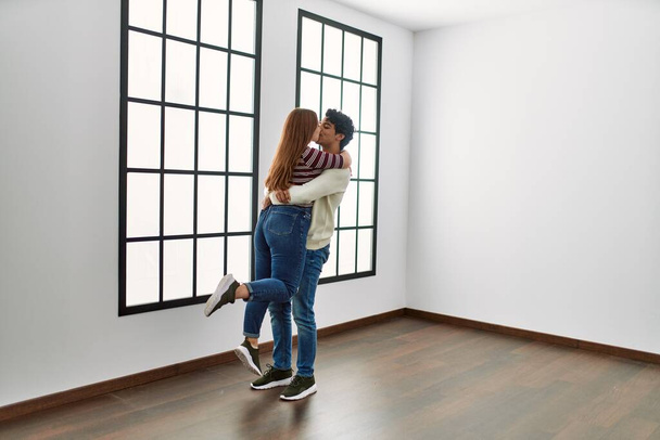 Young hispanic couple kissing and hugging standing at empty new home. - Photo, Image
