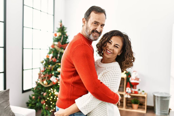 Middle age hispanic couple smiling happy and hugging celebrating christmas at home. - Photo, Image