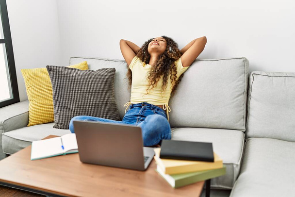 Jovem latina relaxada com as mãos na cabeça usando laptop em casa - Foto, Imagem